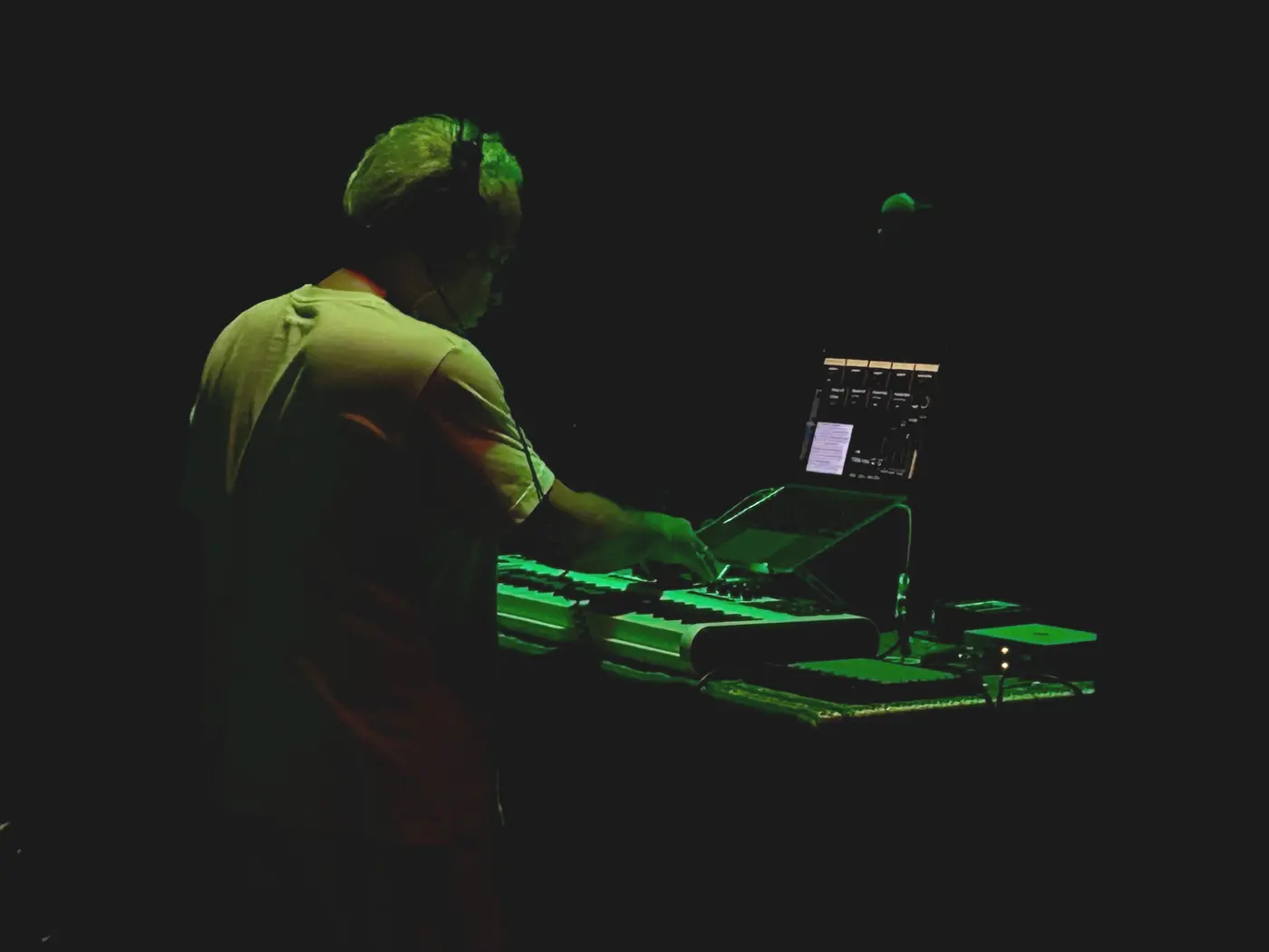 Sam Cutri performing live with keyboard, controllers and laptop under green stage lighting