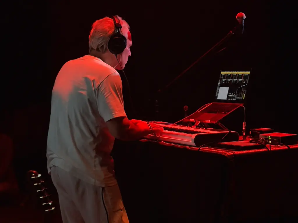 Sam Cutri building a live electronic performance with keyboard, laptop and controllers under red stage lighting