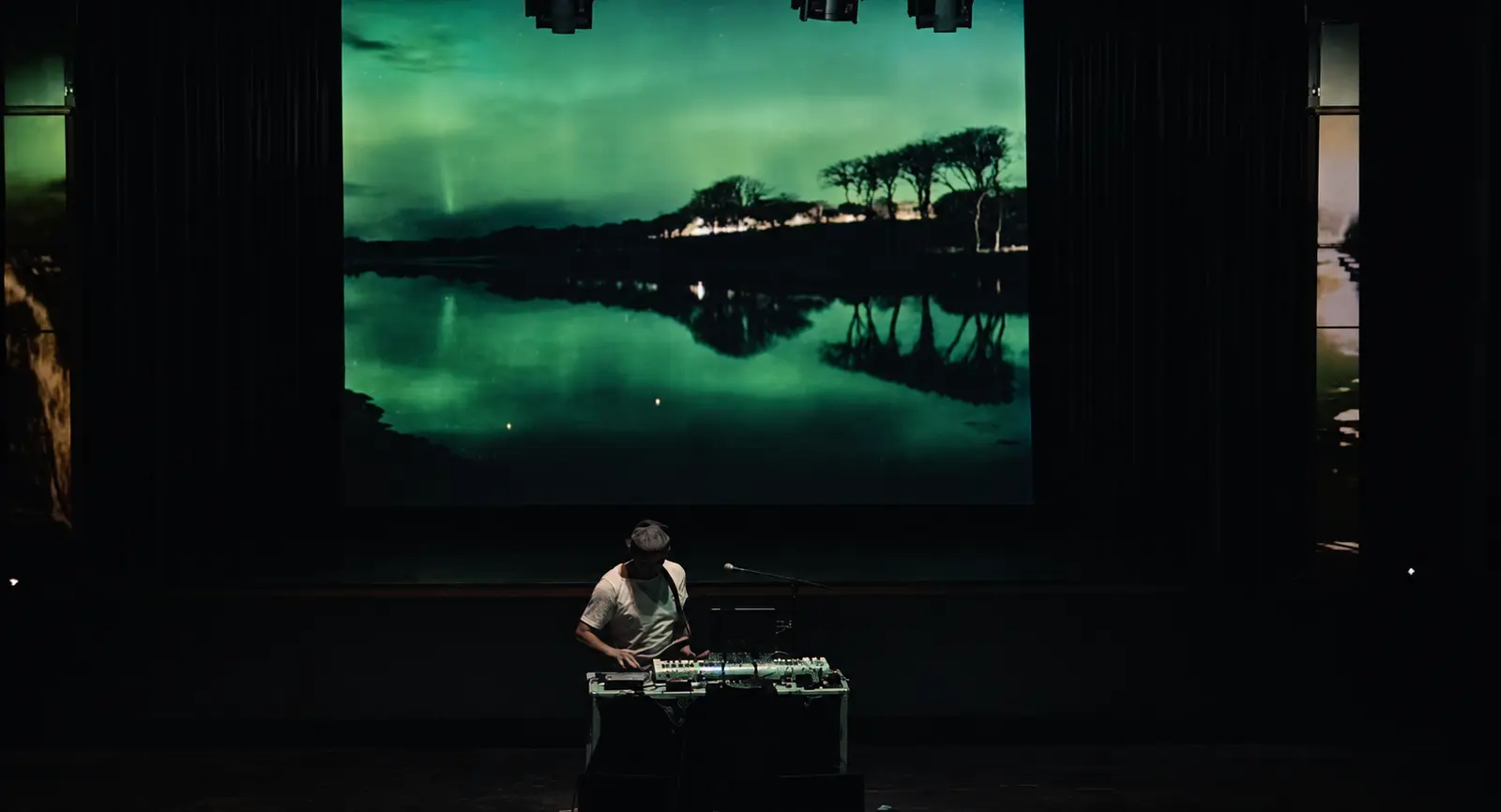 Sam Cutri performing electronic music beneath an immersive projected landscape