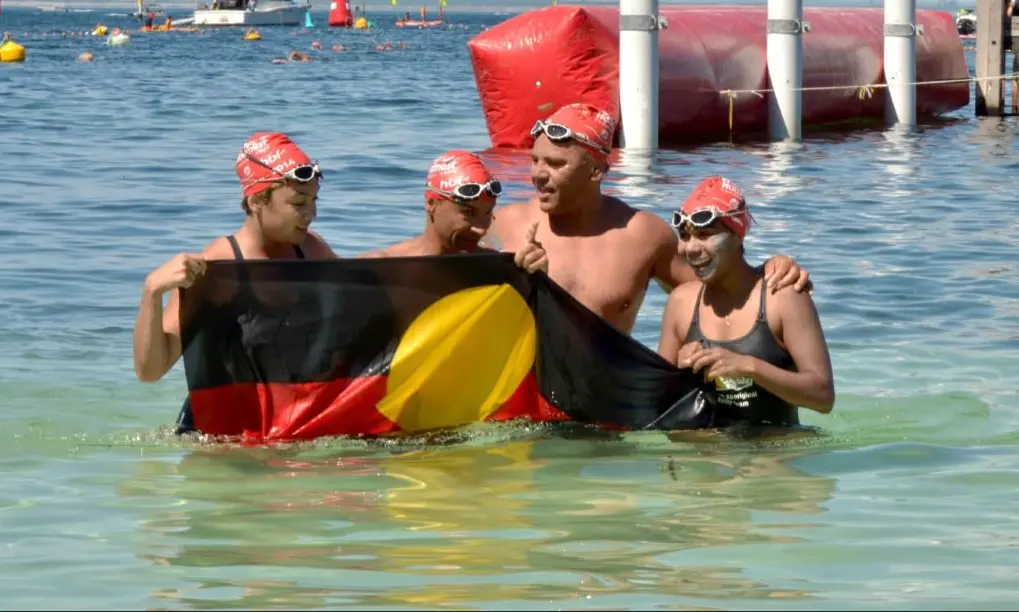 Swimmers holding the Aboriginal flag in the Whadjuk to Wadjemup film cover